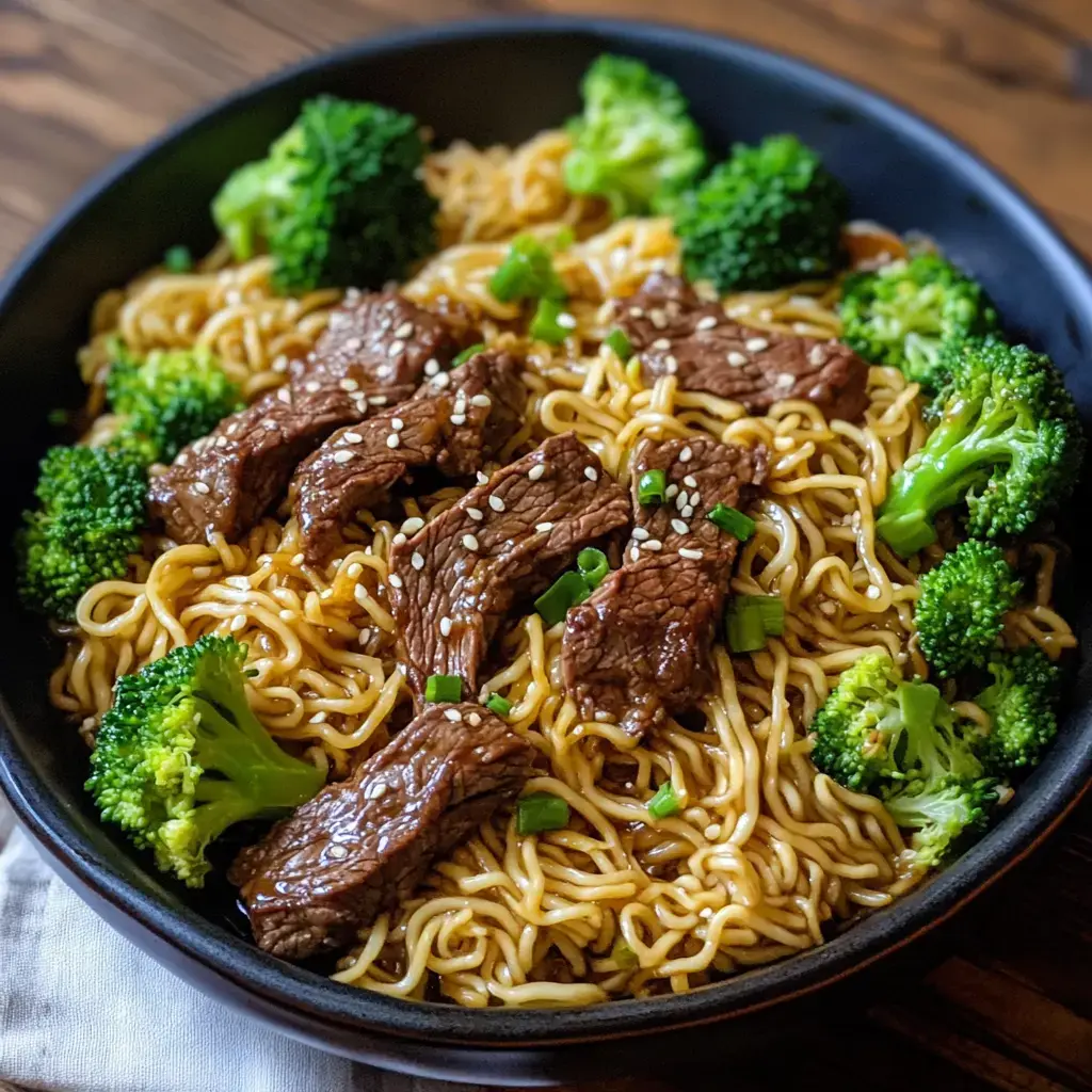 A bowl of stir-fried noodles topped with sliced beef, broccoli, and sesame seeds.