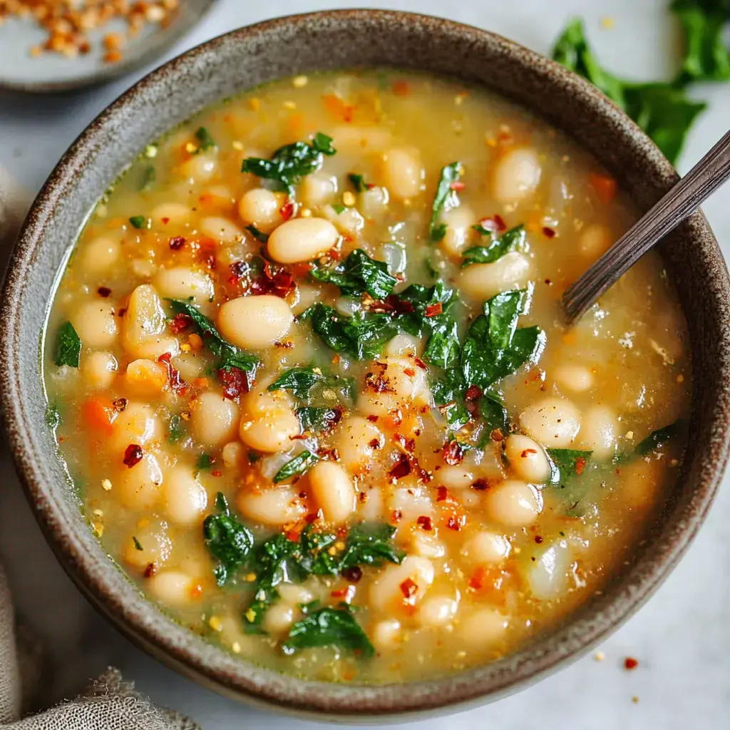 A bowl of white bean soup with spinach and sprinkled red pepper flakes.