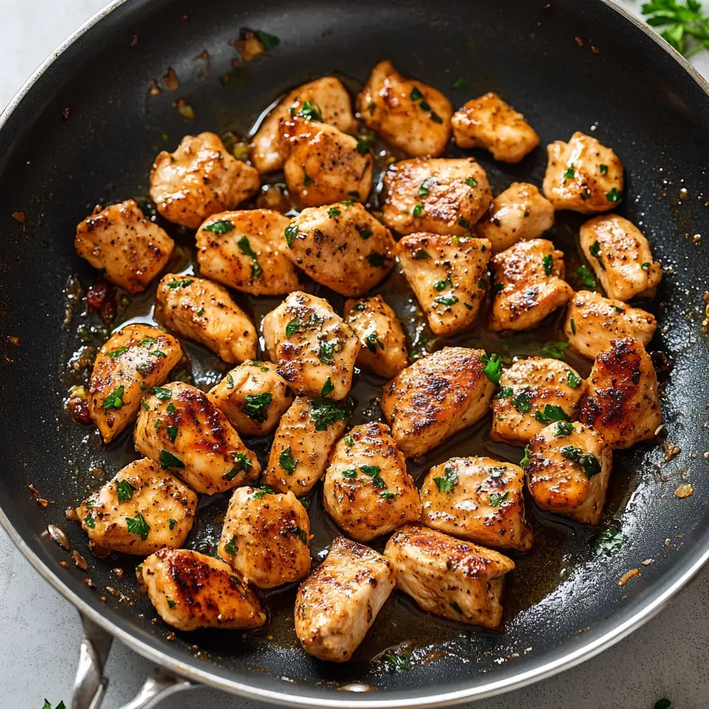 Cooked, diced chicken pieces are browned and garnished with parsley in a skillet.