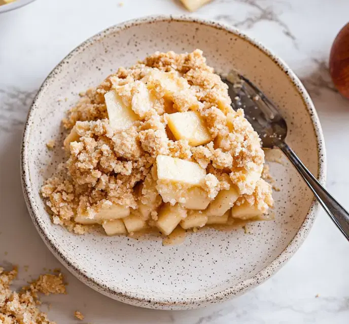 A bowl of apple crisp featuring chopped apples topped with a crumbly streusel topping.