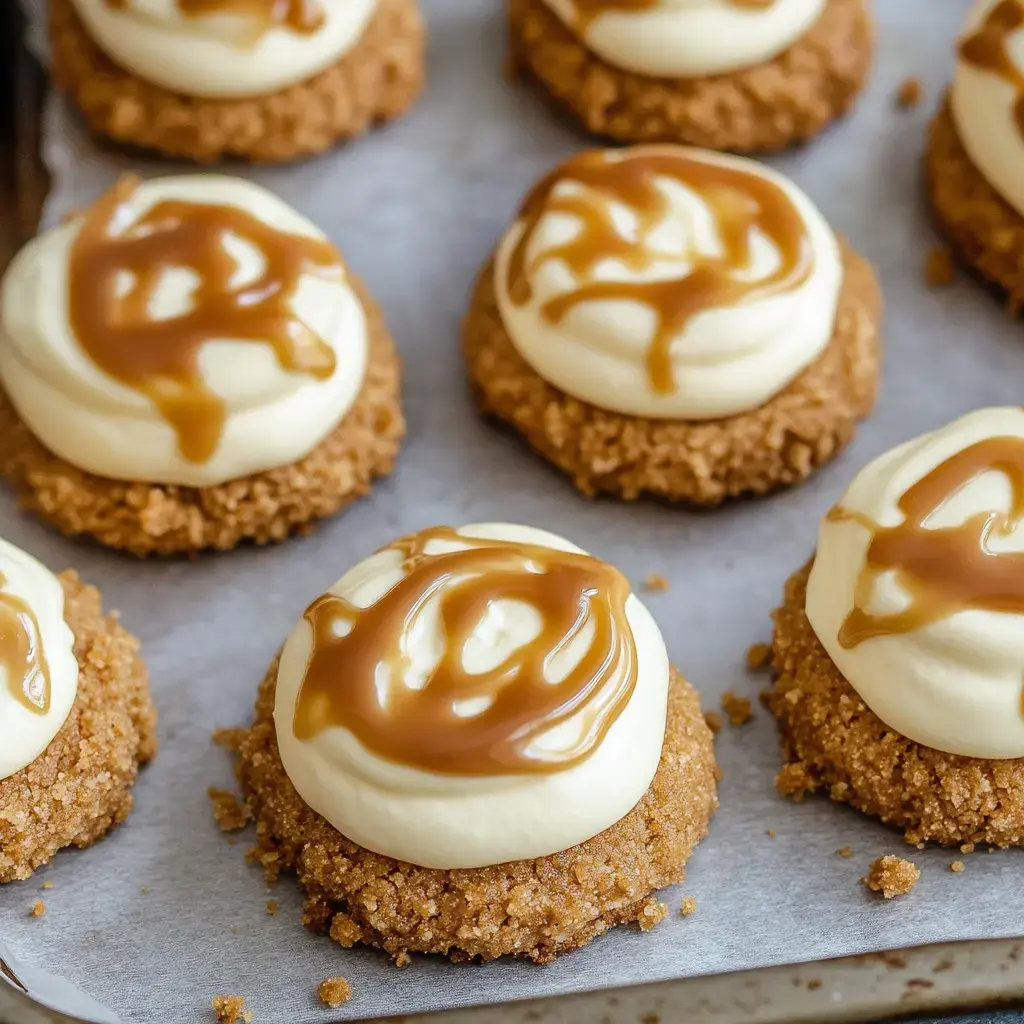 A close-up view of several dessert cookies topped with creamy frosting and a drizzle of caramel sauce, arranged on parchment paper.