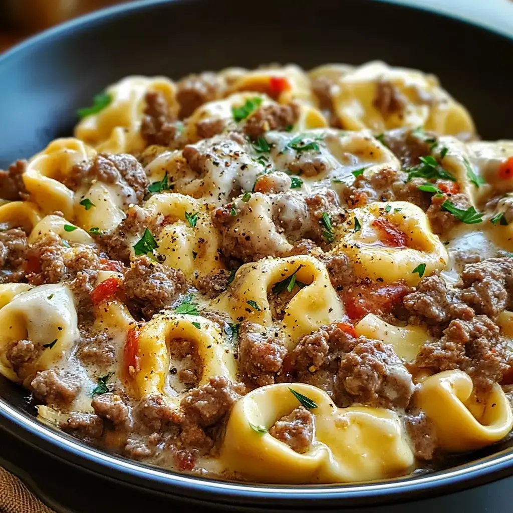 A close-up view of a bowl of creamy pasta with ground beef and herbs, garnished with black pepper.