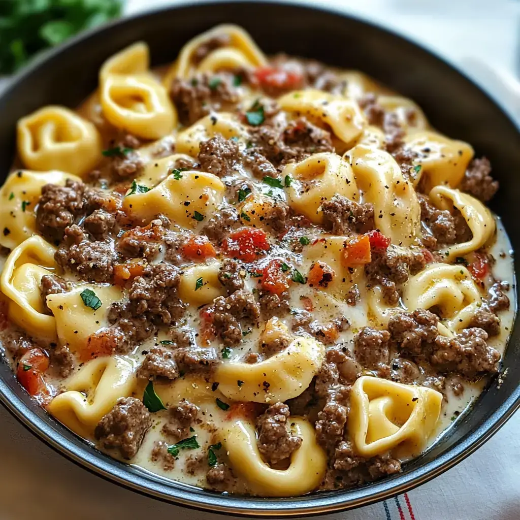 A bowl of creamy pasta with ground beef, diced tomatoes, and fresh parsley.