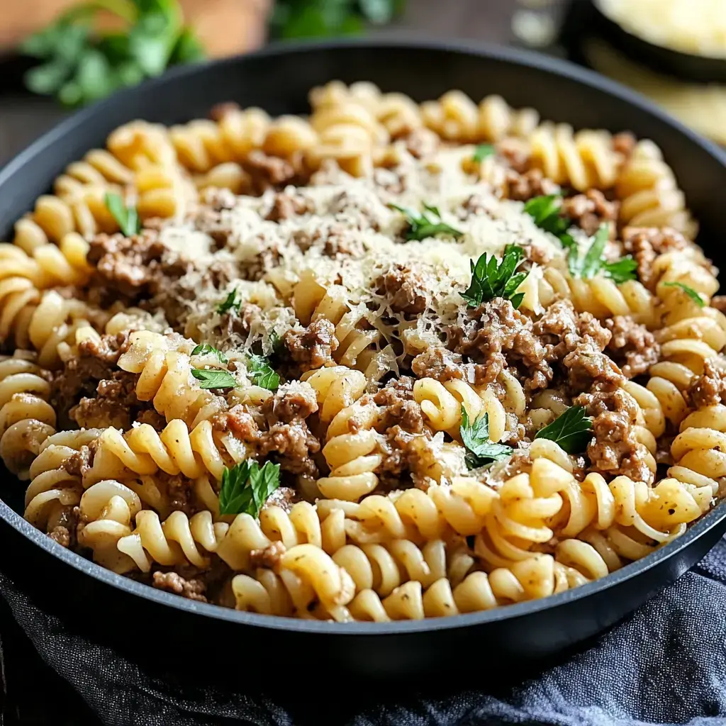 A close-up of a bowl of fusilli pasta mixed with ground meat, garnished with parsley and grated cheese.