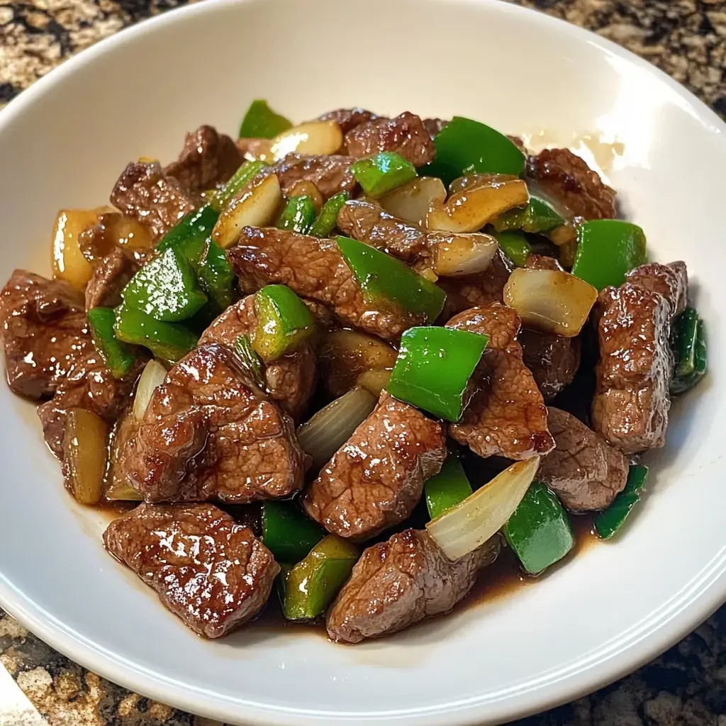 A bowl of sautéed beef pieces mixed with green bell peppers and onions in a savory sauce.