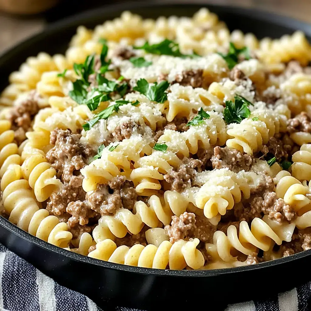 A close-up of a dish featuring rotini pasta topped with seasoned ground meat, parsley, and grated cheese.