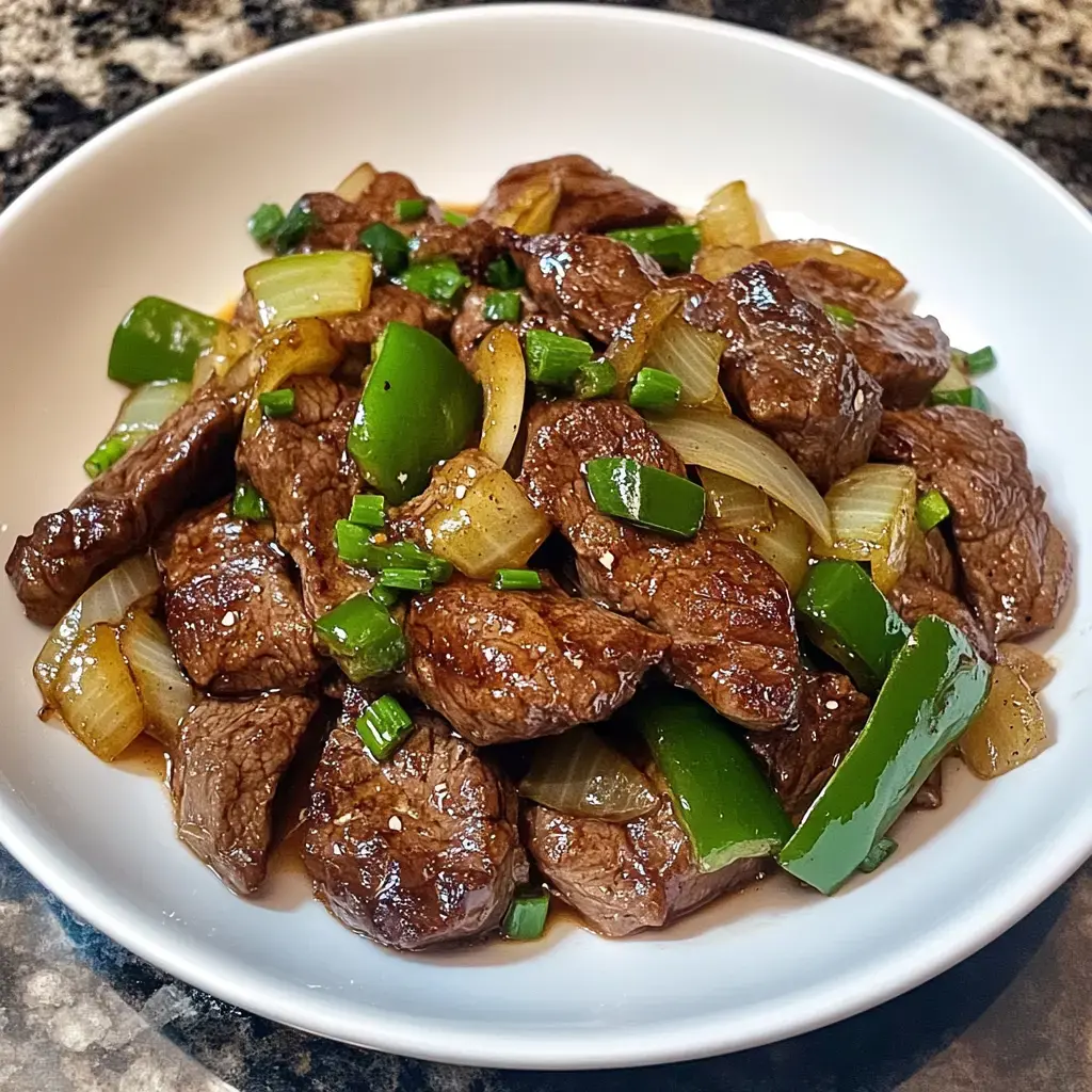 A white bowl filled with sautéed beef, green bell peppers, and onions, garnished with chopped green onions.