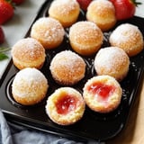 A black tray with a variety of pastries, including a strawberry-filled pastry and a jelly-filled pastry.