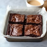 A square of chocolate cake with a cup of coffee next to it.