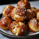 A plate full of bread rolls with sesame seeds on top.