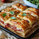 A tray of meat and cheese sandwiches with greens on top.