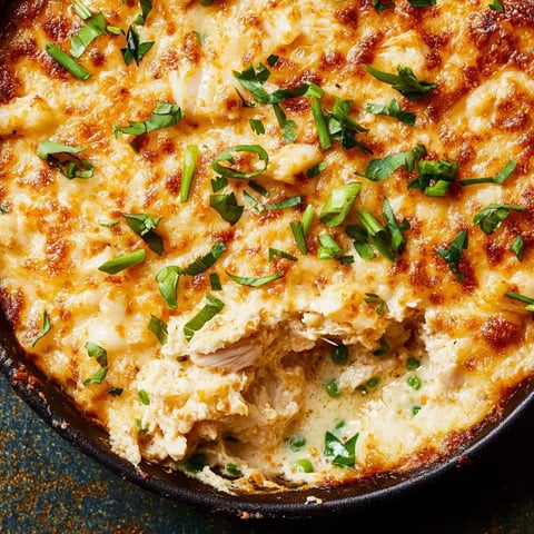 A close-up of a baked dish topped with melted cheese and green herbs, featuring a creamy texture and visible chunks of meat and peas.