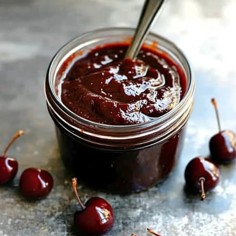 A jar of chocolate sauce with cherries on top.